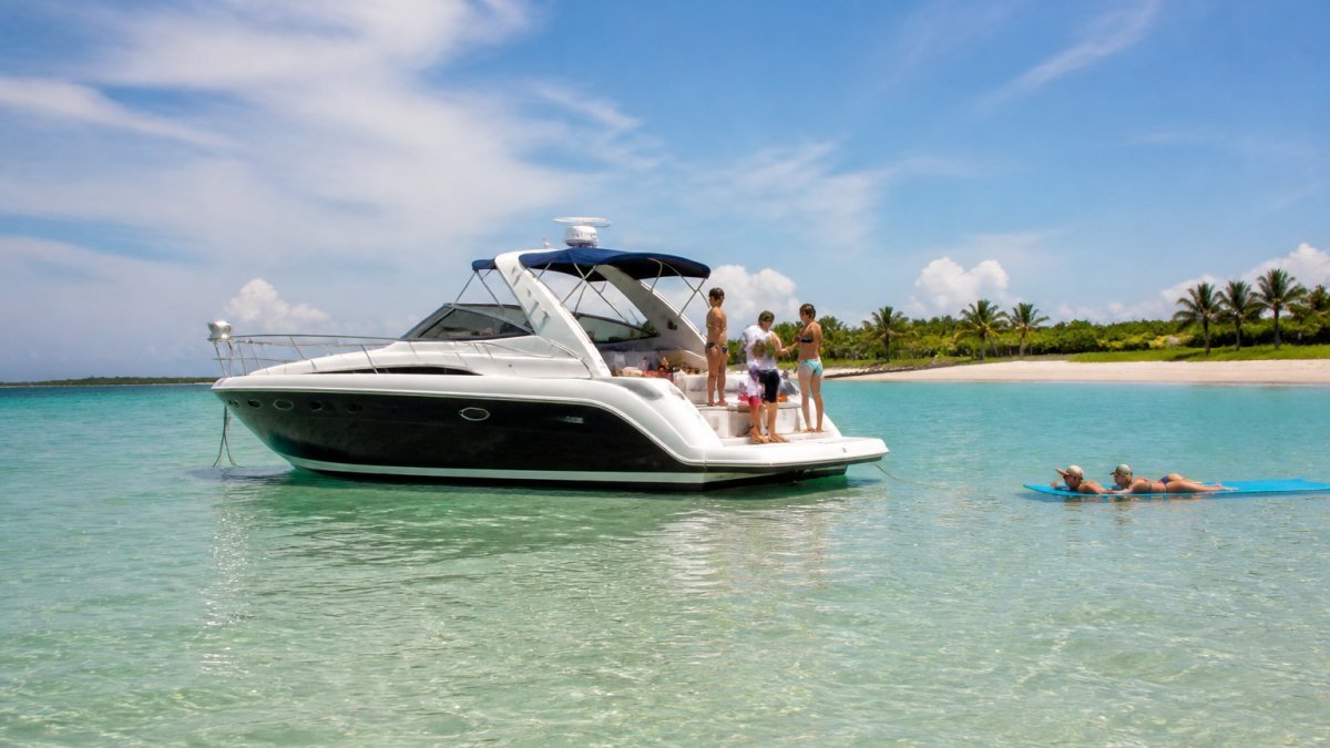 A private charter boat anchored near a sandy South Florida sandbar on a sunny afternoon, with a small group of guests relaxing on deck and calm turquoise water stretching to the shoreline
